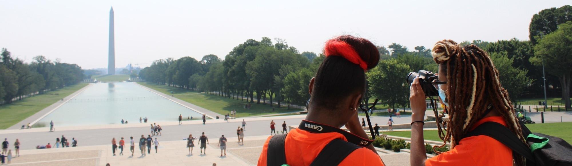 Two girls take photos from the Lincoln Memorial of the Washington Monument.