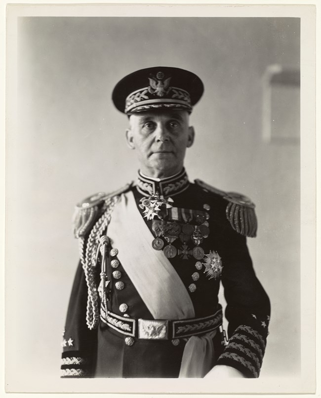 A mature white man in resplendent military garb with cords, sash, and medals.