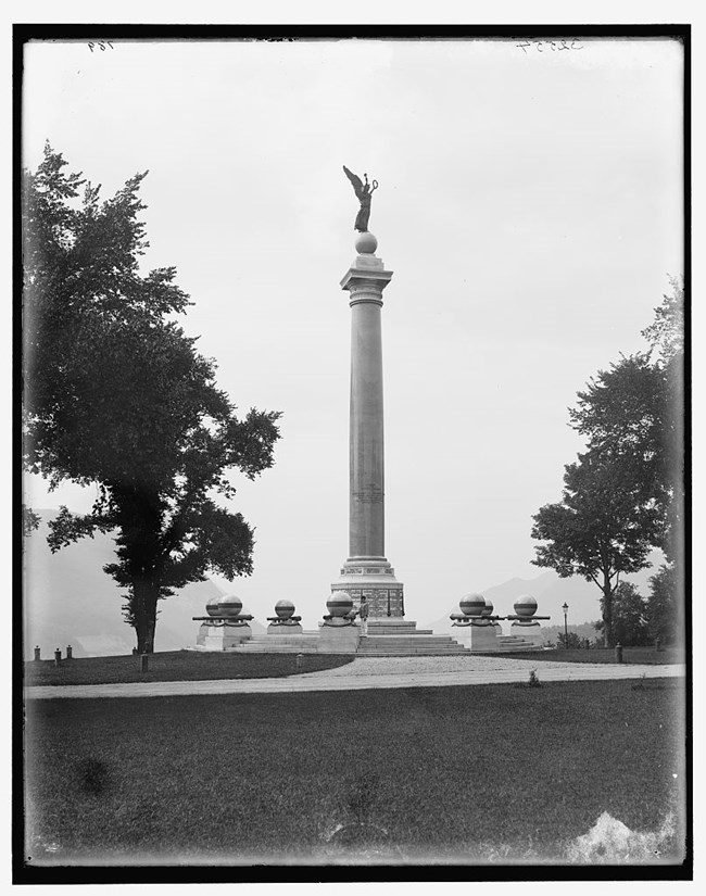 A statue of a winged figure holding a wreath aloft atop a tall column.