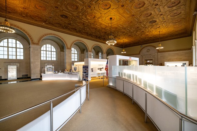 A wide ramp with handrails leads to an information desk in a large room with high ceilings.