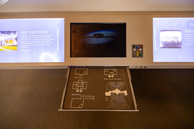A drawer with braille and tactile floor plans is pulled out from under an interactive touchscreen.