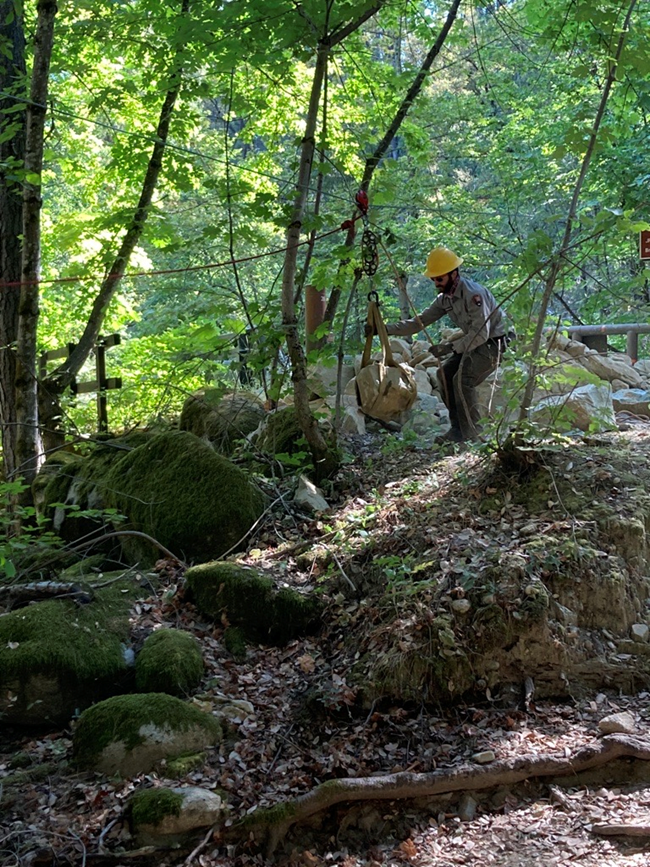 A member of Whiskeytown's trail crew transporting boulders via a rope pully system for use in stabilizing the Brandy Creek Trail.