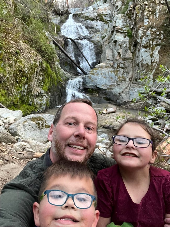 A man, a boy, and a girl pose at the base of Boulder Creek Falls in April 2022.