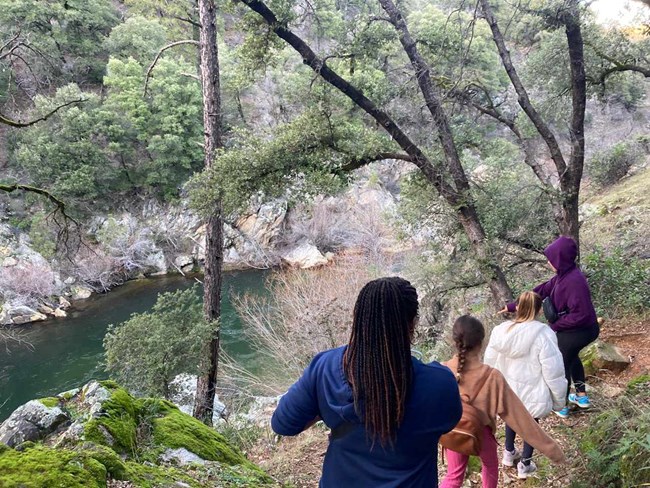 Four females hiking above a green colored stream.