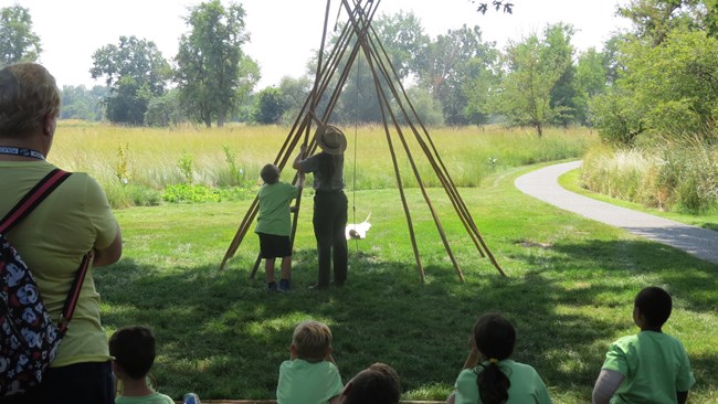 A ranger helps a student place a tipi pole while other students watch