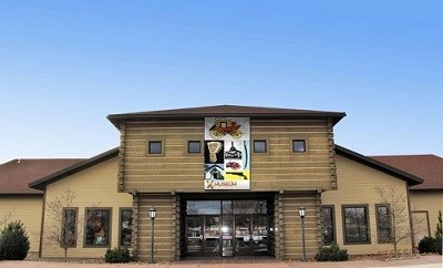 A two story building with the middle section made to look like a log construction but the rest is metal siding. A large banner hangs in front of two sets of glass front doors which says Fort Walla Walla Museum and features historic artifacts