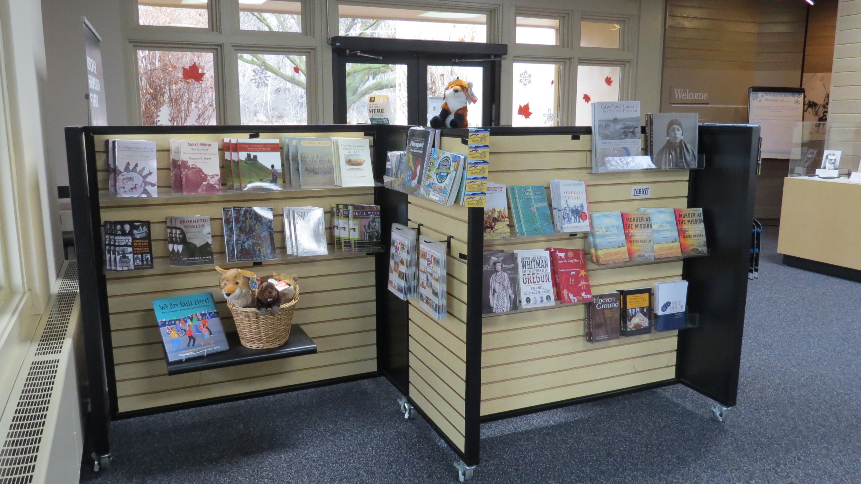Two short mobile shelves of books, collectibles and stuff animals inside a visitor center.