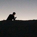 A man resting on the dunes looking at a cell phone.