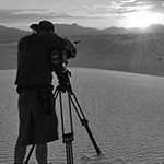 Photographer with tripod on dune.