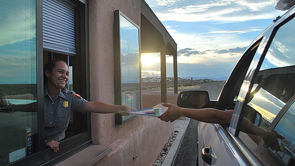A ranger at the entrance station window reaches to give a driver the park map.