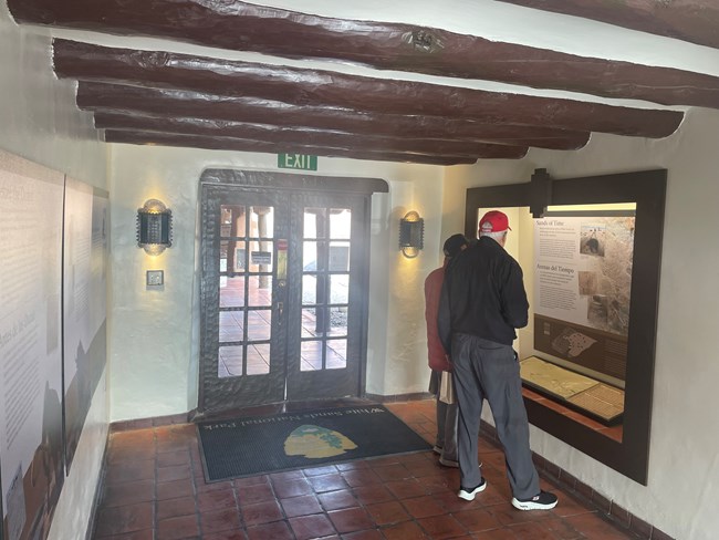 two visitors stand in hallways reading a sign in an alcove. Sands of Time is written on the top. Casted human footprints can be seen in front of the visitors.