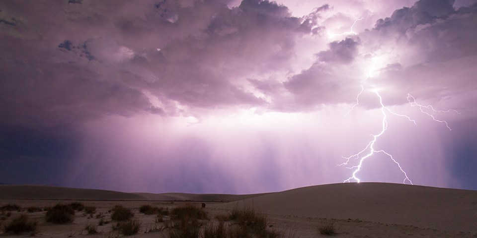 Lightning strikes amidst a bright purple sky and white sand dunes