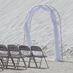 Arch with white fabric and chairs set up in front of dune.