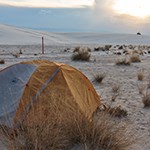 Orange and gray tent set up in area with white sand and grasses