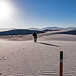One hiker walking on white sand dunes