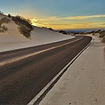 A paved road thorugh white dunes with sunset