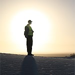 Silhouette of person on dune with sun setting in background.