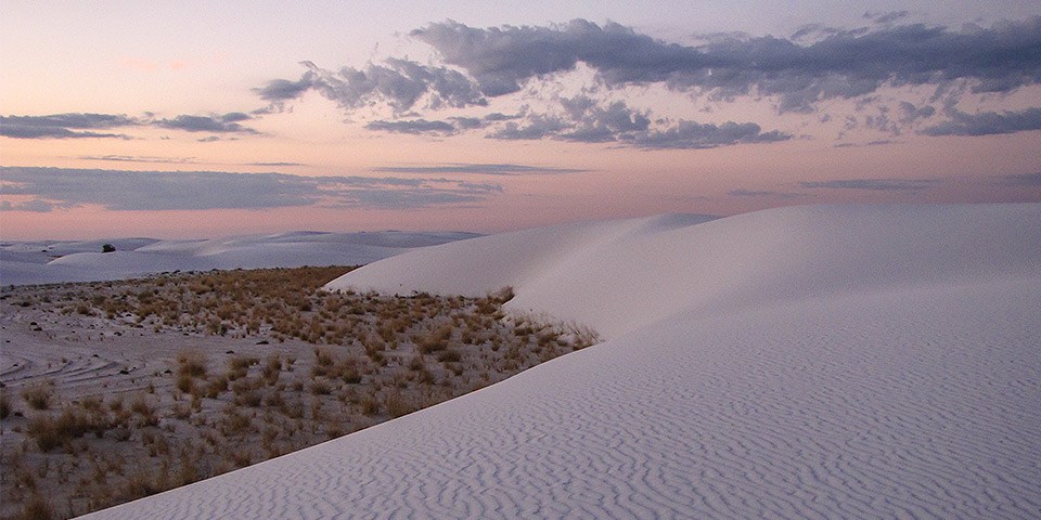sunrise with  light pink and purple clouds in the sky and white sand dunes with ripples in the foreground