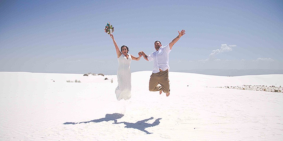A bride and groom jumping into the air holding hands