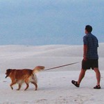A man walking tan dog on leash in white sand
