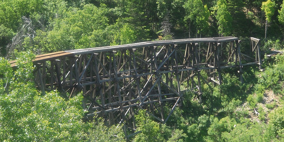 Wooden railroad track in mountains surrounded by green trees.