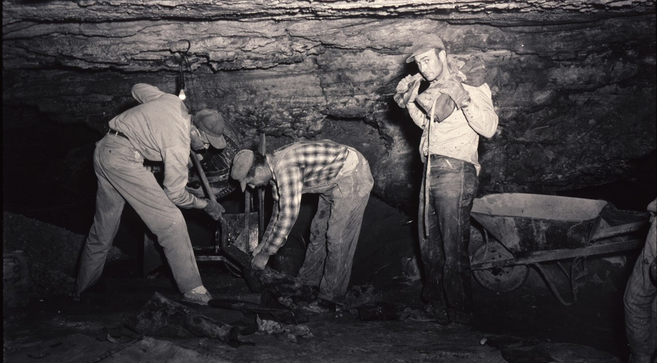 black and white photo of three men in a cave room pouring concrete onto part of the cave floor