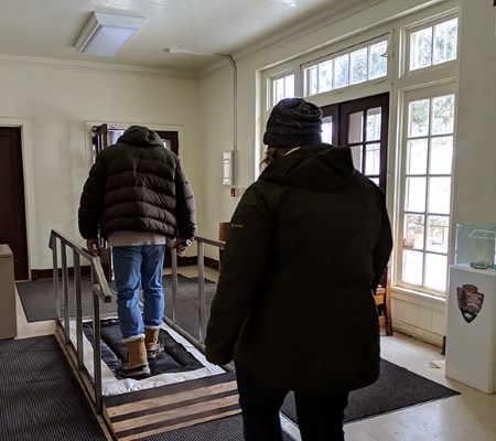 two people walk across a metal bridge with black mats inside a building