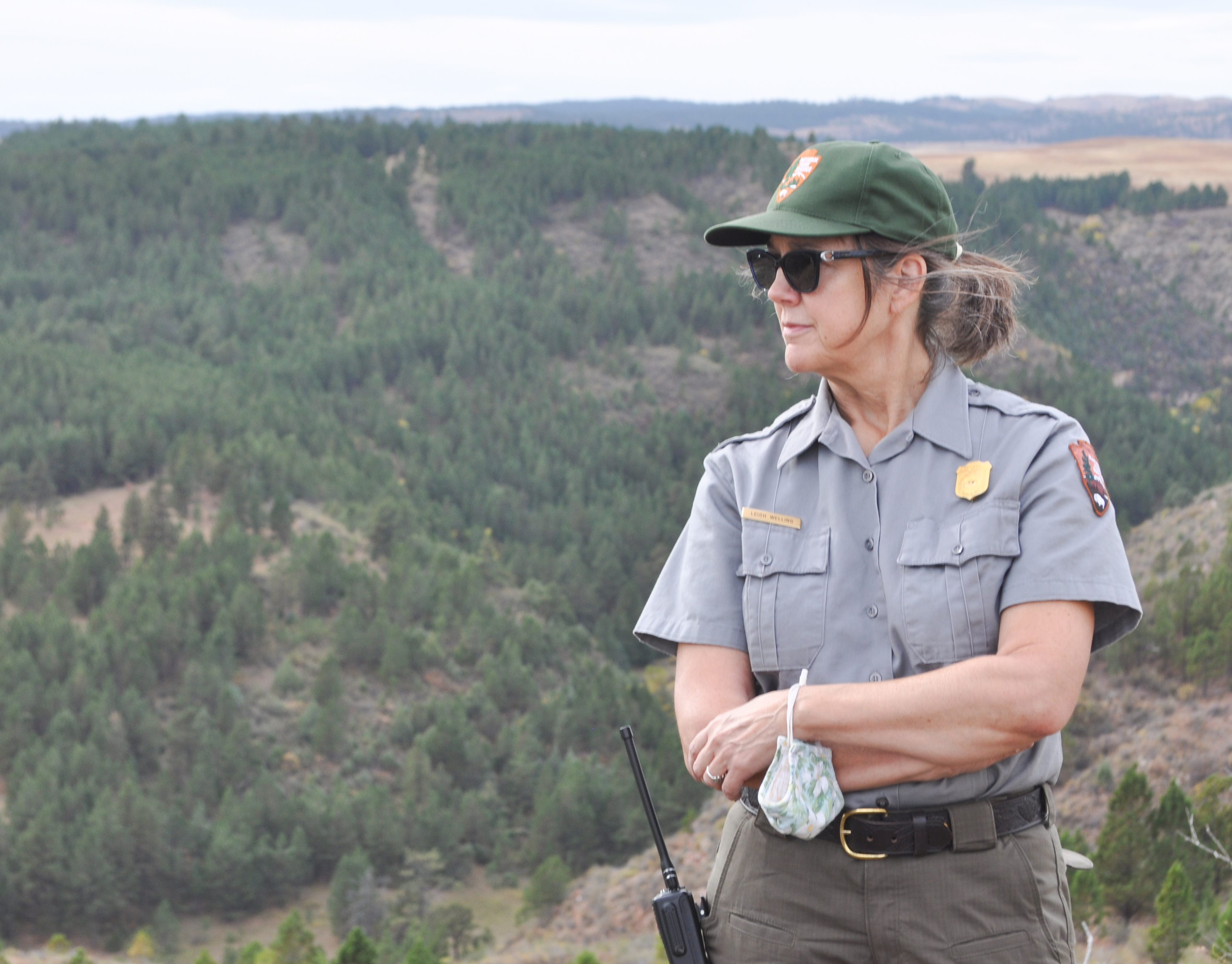 Female park ranger looking to the left with a forested canyon behind her.