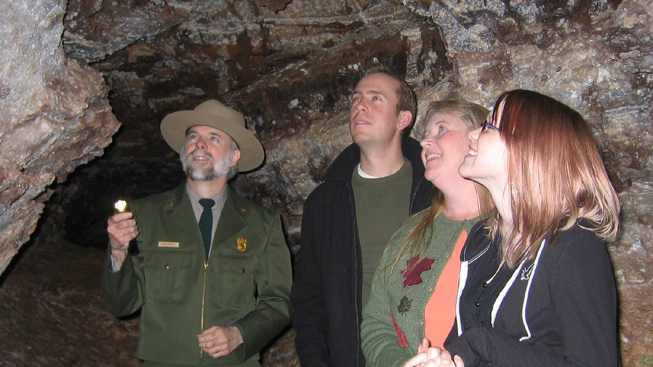 Visitors with a ranger in a dim cave room looking at a formation