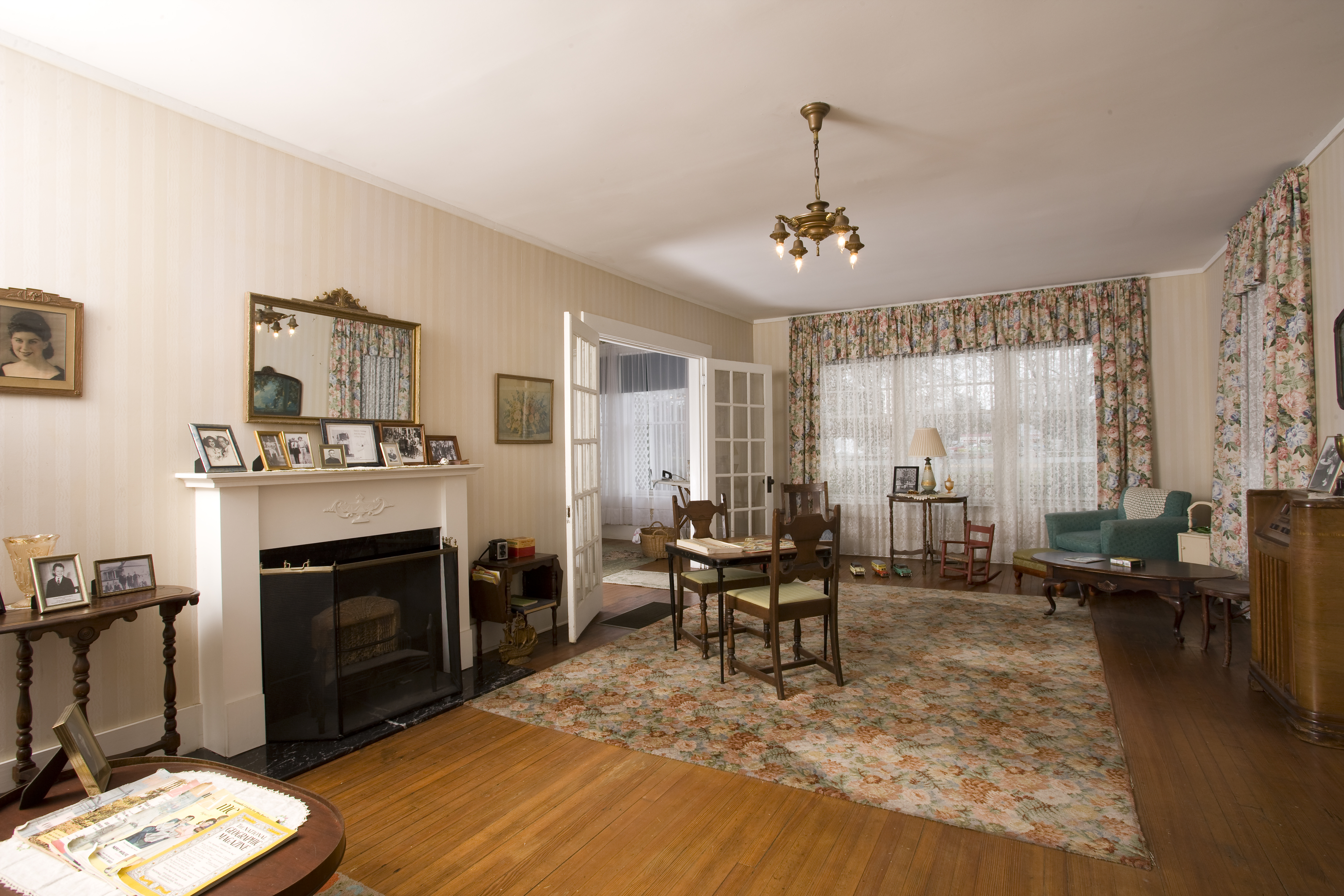The Birthplace Home front room contains a fireplace, table and chairs, family photos and a floor console radio.