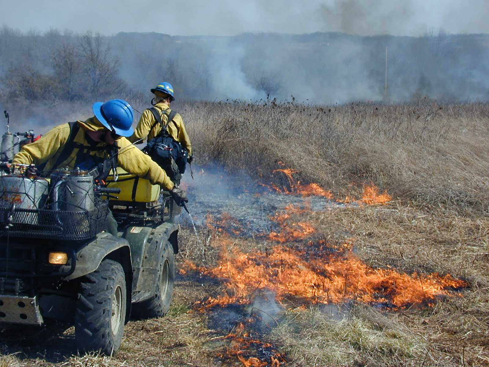 Fire crews burning field during prescribed burn. NPS fire staff burning grasses, one from an ATV another on foot.