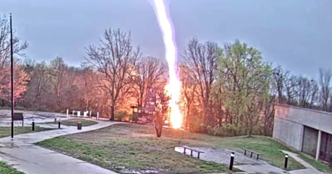 A bolt of lightning strikes the ground in an open area near a building