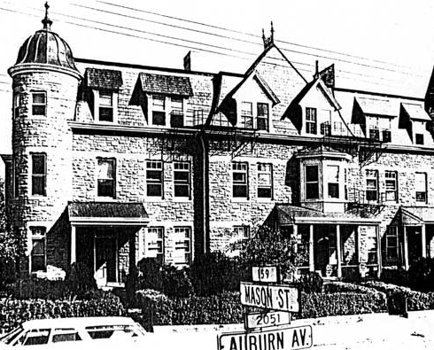 A large three-story building with towering end columns and cars parked on the street in front