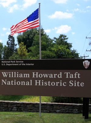 A U.S. flag waving above a sign with text reading William Howard Taft National Historic Site