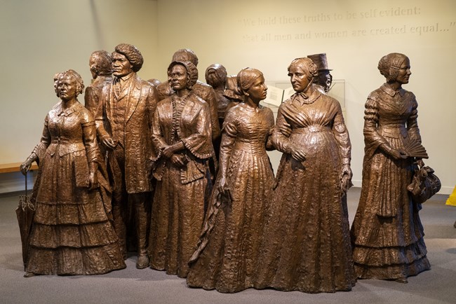 A bronze statue group of men and women in 19th century clothes.