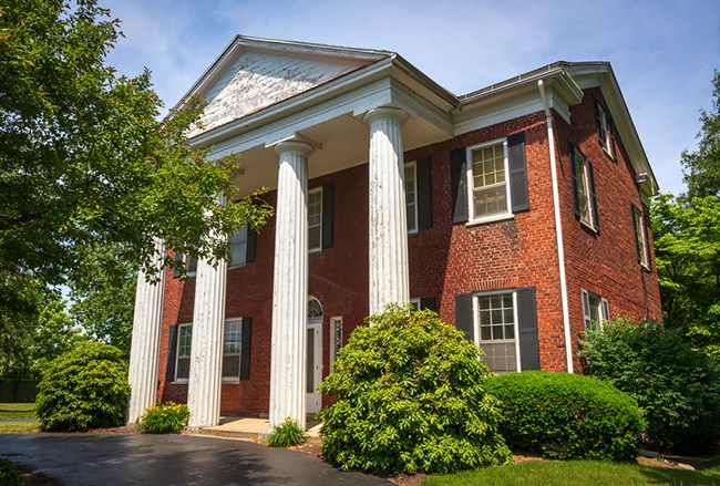 a two-story red brick building with four white columns in front.