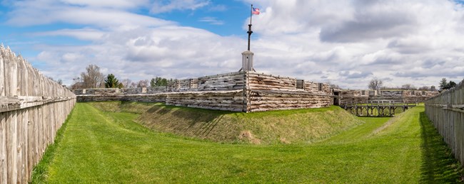 A wooden fort on a grassy hill, flying an American flag