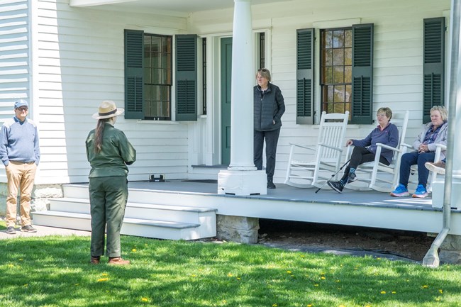 A ranger standing in front of a white house talking to people on the porch.