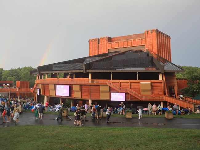 Visitors find their seats on the lawn of the Filene Center after a storm, two rainbows are formed to the left of the theater.