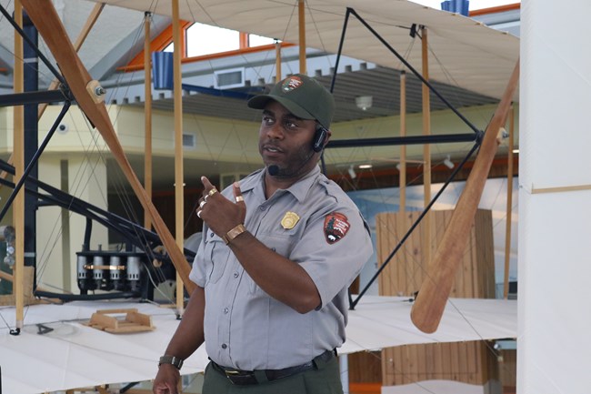 A male ranger in the green and grey uniform with a headset and microphone around his head