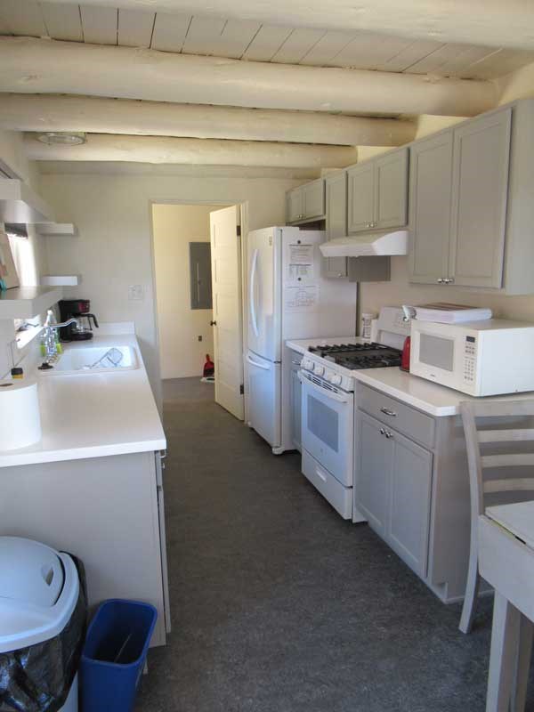 A small kitchen with off white plastered walls, white countertops, light gray cabinets, and a gray floor.