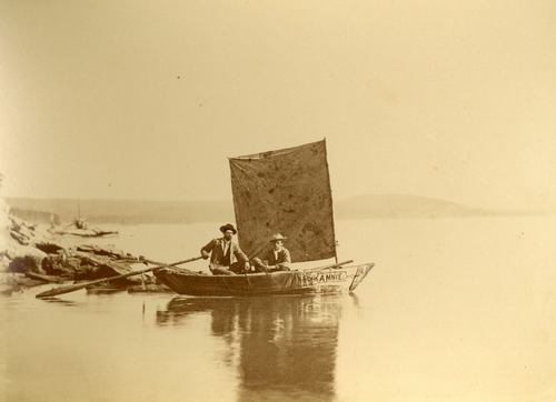 Image of two men in a small sail boat on a large lake.