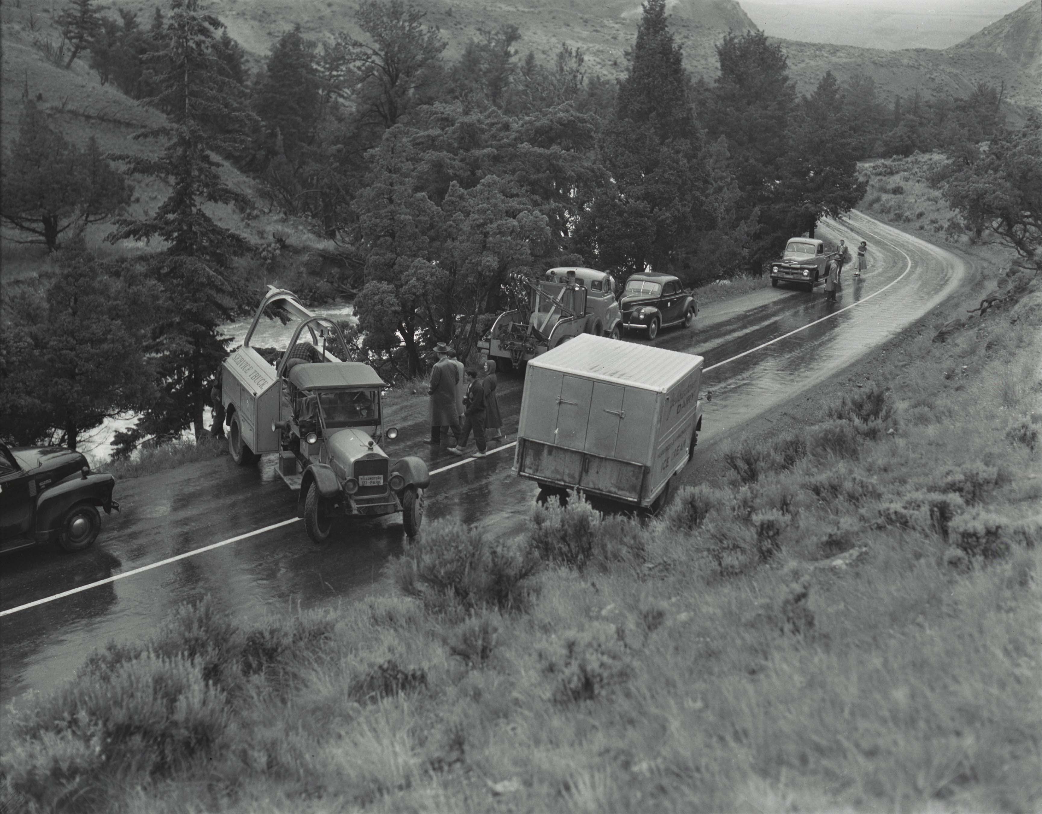 Image of trucks and cars stopped on a wet two-lane road, with people in conversation in the middle of the road.