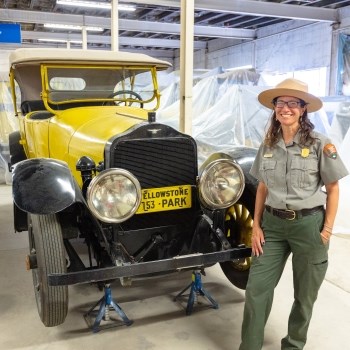 a park ranger standing and smiling next to a historic vehicle