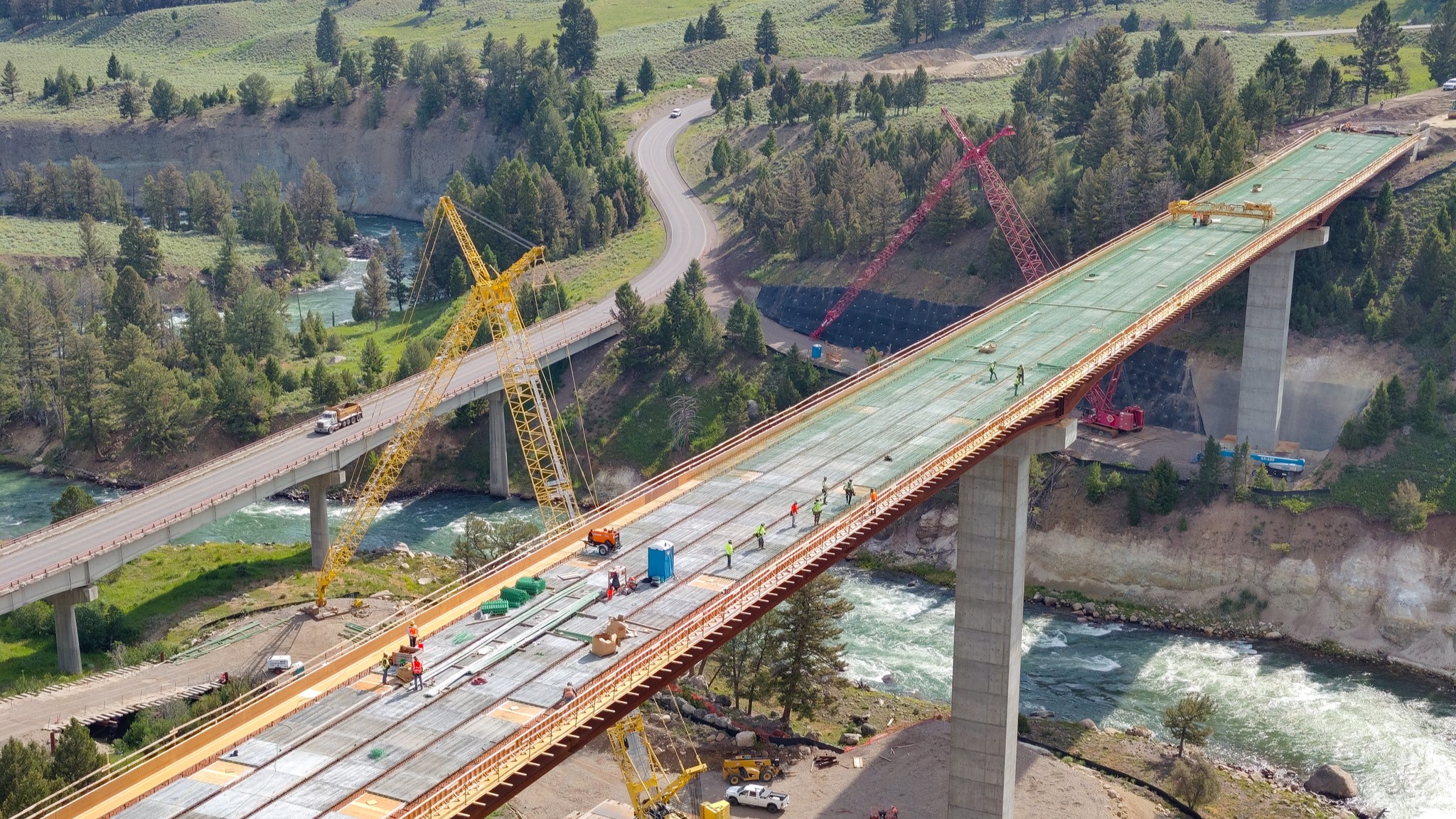 An aerial view of a tall bridge that is under construction and crosses over a winding river.