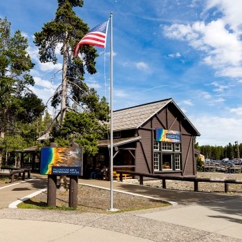 a historic log building with a sign and flag pole in front of it on a summer day