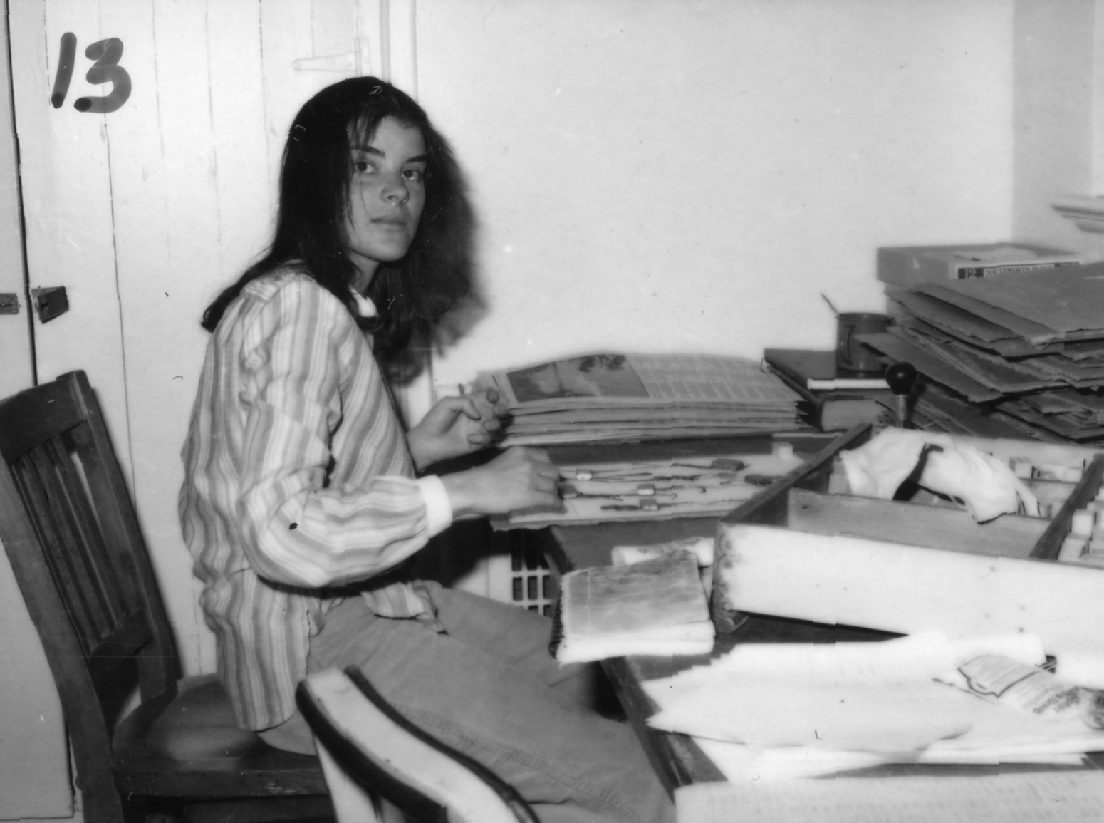 Black-and-white photo of woman sorting through documents at a desk.