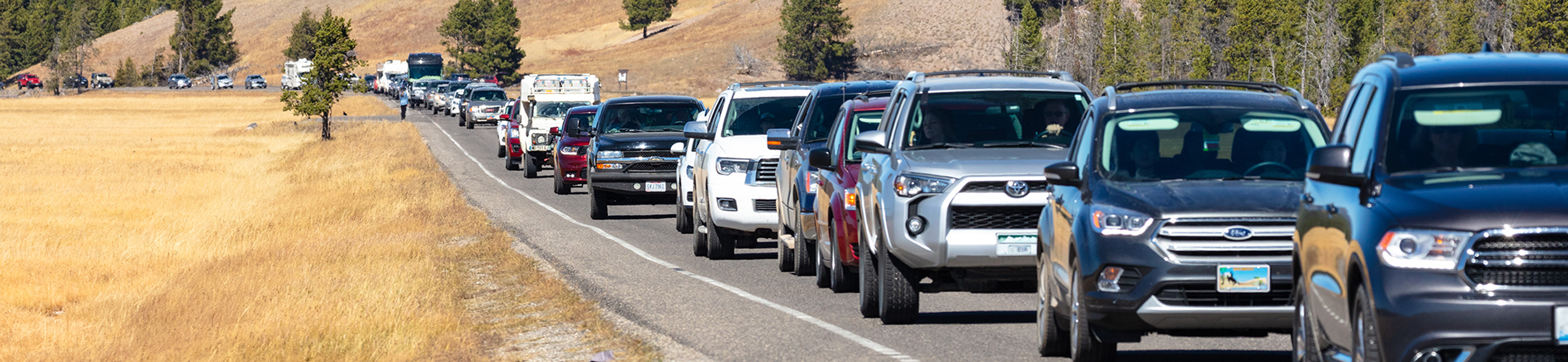 A line of cars on a paved road with mountains in the background.