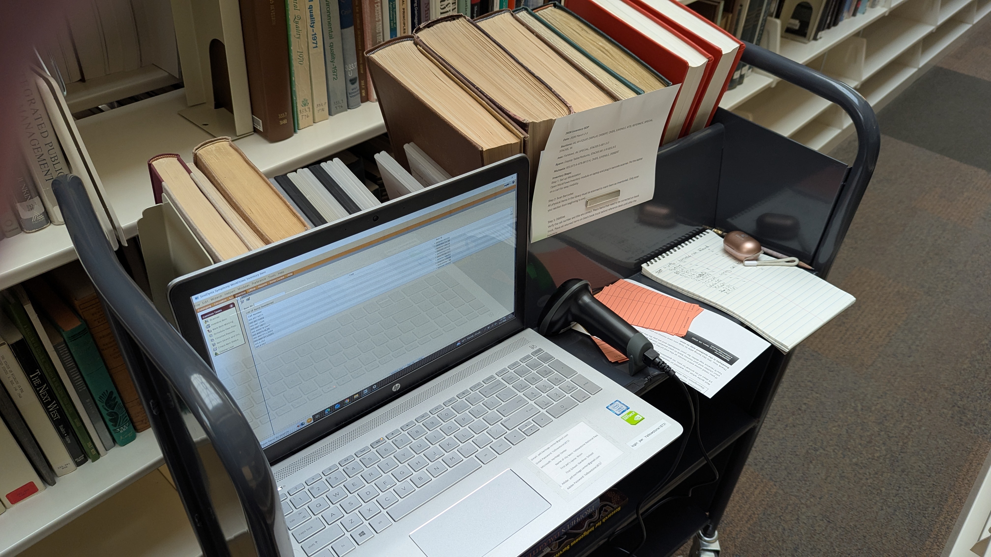 A laptop open to library inventory page and books on a book truck.
