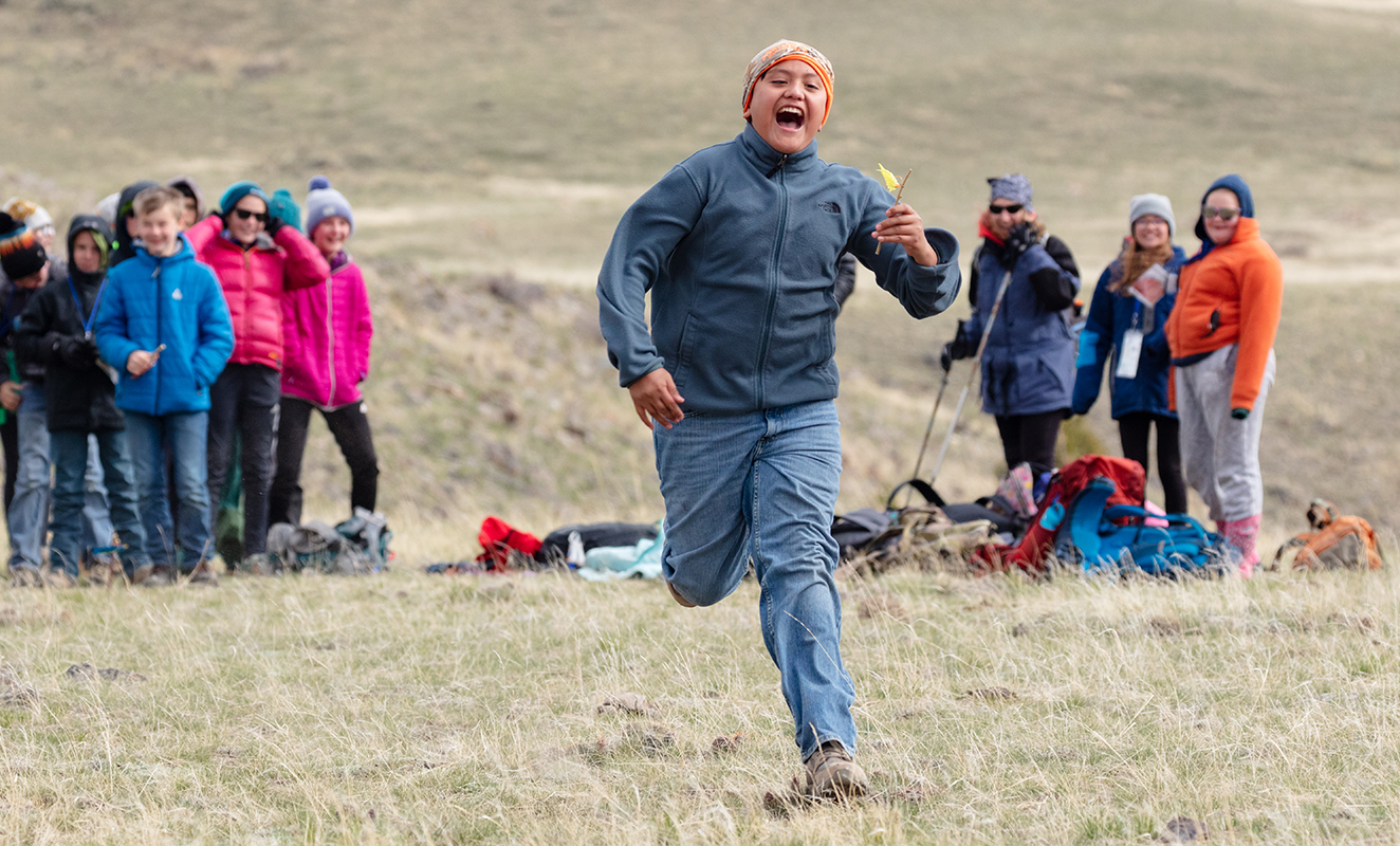 a student runs through a brown grass field while other students look on